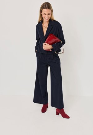 Tumed pinstripe ülikond lühikese jope ja laia säärega pükstega, koos punaste sametist ankle-kingade ja sobiva käekotiga. Kuldse ahelaga kaunistused.