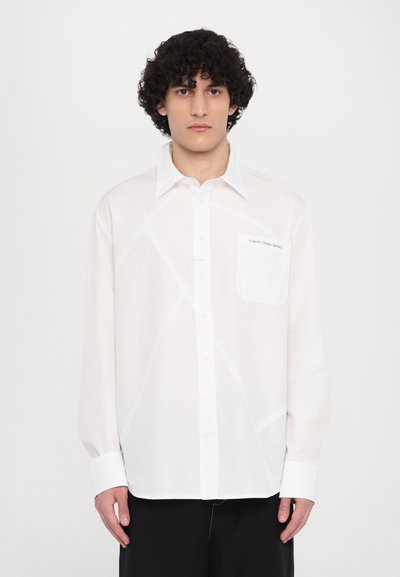 Camisa blanca de botones con una textura suave y patrones de costura geométricos. Presenta un bolsillo en el pecho izquierdo con la marca del logo. Mangas largas.