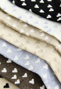 Bunte Socken in Schichten angeordnet, mit kleinen Herzmustern. Die Farben umfassen Schwarz, Weiß, Beige, Hellblau und Braun. Weiche Textur.