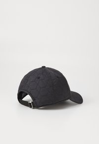 Black quilted cap featuring a hexagonal pattern, curved brim, and adjustable strap at the back for a secure fit.