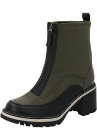 Botín de tobillo verde y negro con un tacón grueso, materiales de lona y cuero, cierre de cremallera y suela texturizada con profundas huellas.