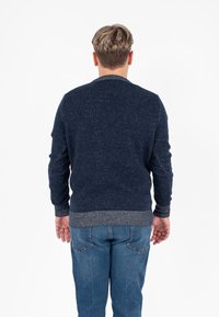 Maglione di colore navy a maglia con un design testurizzato, caratterizzato da orlo e polsini a coste a contrasto. Indossato su jeans blu, visto da dietro.