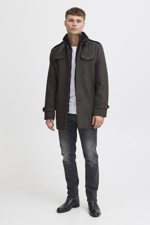 Grå uldblandingsfrakke med en struktureret design, skulderlapper, knaplukninger og sidelommer, båret over en hvid skjorte og mørke jeans.