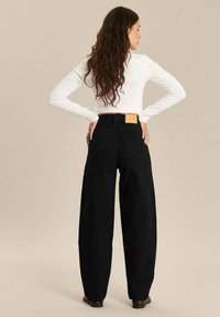 Zwarte wijde spijkerbroek van denim, met een hoge taille en een tan leren label achter, gestyled met een aansluitend wit longsleeve top.