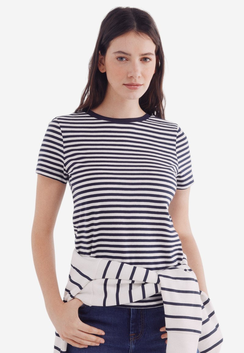 Marineblå og hvidstribet kortærmet t-shirt med rund hals. En lys top er sat casual om taljen.