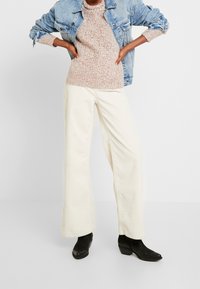 Vaaleanbeiget leveälahkeiset ribbihousut yhdistettynä pehmeän vaaleanpunaiseen teksturoituun neulepaitaan ja vaaleansiniseen farkkutakkiin. Mustat nilkkurit täydentävät asun.