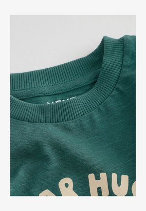 Felpa in cotone verde scuro con collo a girocollo a coste e design testuale beige. Il tessuto ha una sottile texture.