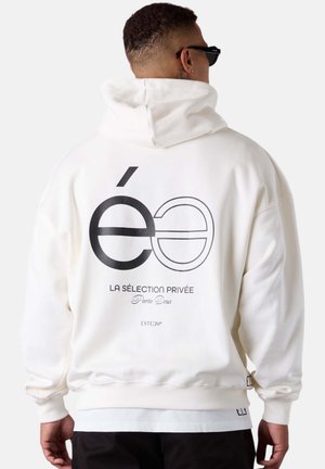 Haut à capuche blanc avec un grand design graphique en texte noir au dos. Le tissu semble doux avec une coupe décontractée et des poignets côtelés.