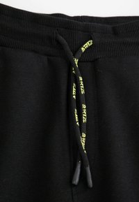 Czarne dresy z teksturowanej tkaniny, elastycznym pasem i kontrastującym żółtym sznurkiem do regulacji, z nadrukowanym logo.