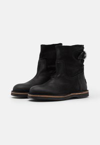 Botas de tobillo de ante negro con punta redonda, panel elástico lateral y detalle de hebilla plateada, que cuentan con una suela marrón en contraste.
