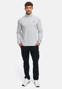 Sudadera de cuello alto gris con un diseño ajustado, que presenta un pequeño logotipo redondo. Combinada con pantalones cargo negros y zapatillas blancas.