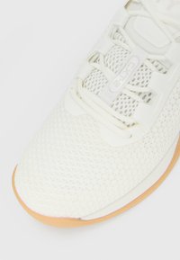 Hvide åndbare mesh sneakers med cremefarvede snørebånd og gummigummi sål, viser top-front udsigt og 'CXT12' branding på tungen.