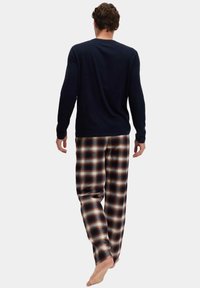 Camicia a maniche lunghe blu navy abbinata a pantaloni da pigiama in cotone a quadri nei toni marrone, beige e blu, con una vestibilità comoda e vita elastica.