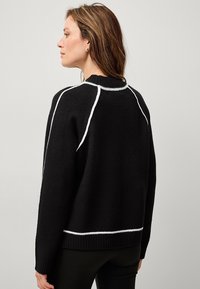 Maglione nero con cuciture bianche accentate sulle spalle e sull'orlo. Presenta un colletto e dei polsini a coste e una vestibilità comoda.