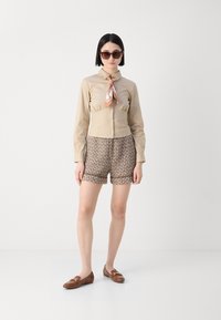 Beige button-up shirt with a cinched waist, paired with patterned brown shorts. Brown loafers with hardware accents and oversized sunglasses.