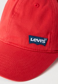 Κόκκινο βαμβακερό καπέλο μπέιζμπολ με μπλε έμβλημα λογότυπου Levi's. Το καπέλο διαθέτει δ ομημένη κορυφή και ραμμένες λεπτομέρειες στο γείσο.