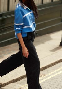 Jasnoniebieski sweter z białymi paskami, uzupełniony czarnymi szerokimi spodniami z korduroju. Sweter ma kołnierz i luźny krój.