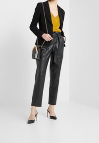 Zwarte op maat gemaakte blazer, mosterdkleurige satijnen cami, zwarte leren high-waisted broek en zwarte puntige hakken. Kleine crossbody tas met gouden accenten.