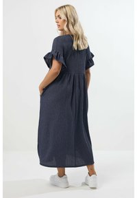 Marine gestreiftes Maxikleid mit kurzen, volantsäugigen Ärmeln, geraffter Taille, Seitentaschen und fließender Silhouette. Tragen mit weißen Sneakern.