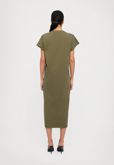 Olive green knee-length dress made from soft fabric, featuring short sleeves and a simple design. Paired with black heeled shoes.
