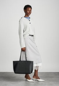 Sac de transport en cuir noir avec deux poignées, design minimaliste, surface texturée, placé contre un fond clair. Les accents comprennent des détails de couture.