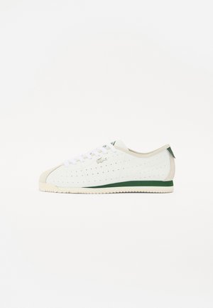 Zapatillas blancas con diseño perforado, detalles en verde y punta de color beige. Cuentan con cordones blancos, una suela texturizada y un logo de la marca.