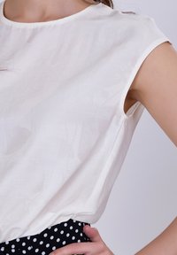 Haut blanc à manches courtes avec un motif floral subtil, associé à une jupe à pois noire. Tissu léger et coupe décontractée.