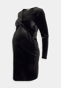 Svart sammet långärmad gravidklänning med samlad twistdetalj vid bysten och figurnära knälång siluett på vit bakgrund.