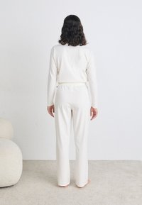 Ensemble de loungewear en coton blanc comprenant un haut à manches longues et un pantalon à taille élastique. Texture lisse et coupe décontractée, vu de dos.
