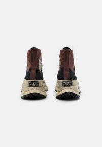Vyšší tenisky s černo-hnědým textilním svrškem, vyčnívající znakem, béžovou mezipodešví a strukturovanou černou gumovou podešví.