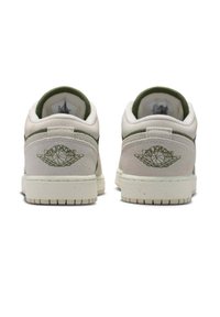 Tył niskich sneakersów w jasnobeżowym i zielonym kolorze. Wykonane z zamszu, z zielonymi akcentami i wyszywanym logo na pięcie. Podeszwa o fakturowanej powierzchni.