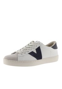 Baskets blanches avec un capuchon en suède gris et un accent en forme de V bleu marine, dotées de lacets plats et d'une semelle en caoutchouc.
