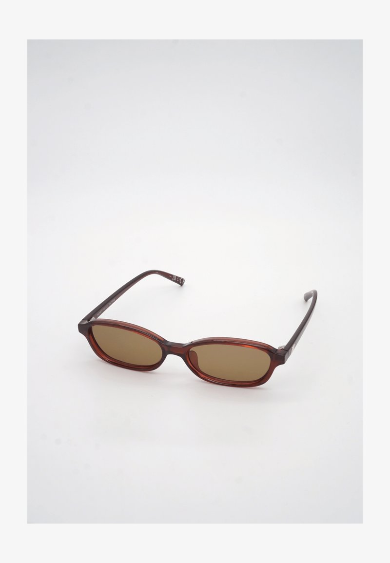 Καφέ ορθογώνια γυαλιά ηλίου με λεπτούς σκούρους καφέ βραχίονες που ακουμπούν σε λευκή επιφάνεια.