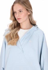 Világoskék esőkabát vízlepergető anyagból, kapucnival, patentos záródással és egy apró logóval a mellrészen.