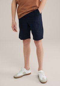 Marinblå shorts i bomullsblandning, med sidofickor och rak skärning. Tillsammans med vita och grå sportskor.