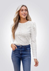Witte lange mouwen blouse met oogjesstructuur en geplooide schouders, gecombineerd met blauwe hoge taille jeans. Soepele stof, fijn patroon detail.