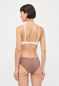 Bralette en crème clair avec bretelles réglables, design structuré. Associé à des culottes de bikini brunes sans couture, texture lisse et coupe classique.