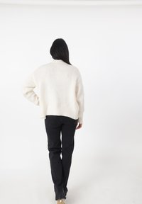 Creme gebreide trui met een ontspannen pasvorm, geribbelde onderkant en verlaagde schouders, gecombineerd met zwarte rechte broek op een model.
