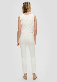 Witte mouwloze top met bloemenborduursel, gecombineerd met strakke witte jeans. Licht textuur, cropped ontwerp en platte sandalen met metalen accenten.