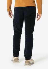 Navy Cargo-Hosen aus Baumwolle mit schmaler Passform, ausgestattet mit Seitentaschen und einer strukturierten Oberfläche. Getragen mit hellen Sneakers.