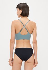 Sport-BH in Türkis mit überkreuzten Trägern, kombiniert mit einem schwarzen Bikiniunterteil. Glatte Textur mit minimalem Design. 