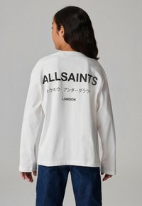 Pikad varrukad valge T-särk, mille seljal must tekst: "ALLSAINTS" ja "LONDON." Puuvillane materjal, lõdva istuvusega, ümmargune dekoltee ja veidi langetatud õlgadega.
