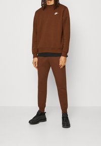 Brown Nike sweatshirt with a crew neckline, ribbed cuffs, and matching joggers. Black sneakers with textured soles and accent details.