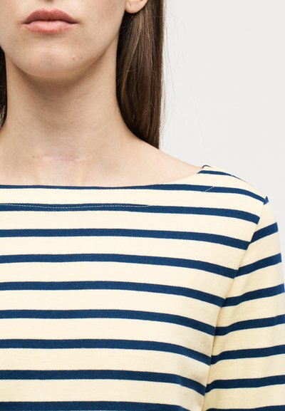 Γυναίκα με ίσια καστανά μαλλιά που φοράει μπλούζα με κρεμ και ναυτικό μπλε ρίγες, δείχνοντας μια αχνή ουλή στον κάτω λαιμό.