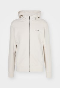 Felpa con zip beige di Calvin Klein, con una texture liscia, cappuccio a due strati, tasche laterali e logo ricamato sul petto.