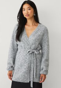 Cardigan grigio lavorato a maglia con design avvolgente, cintato in vita, con maniche lunghe e una consistenza morbida e pelosa.