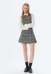 Vestido a rayas en blanco y negro con falda acampanada y un corsé ajustado, combinado con una camisa blanca con cuello y mocasines negros.