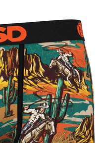 Des cowboys chevauchent des chevaux et font tournoyer des lassos dans un paysage désertique avec des cactus et des montagnes rocheuses sur un tissu à motifs colorés.