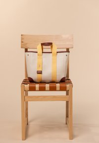 Sac en toile avec des anse jaunes et des accents en cuir marron, en forme rectangulaire, exposé sur une chaise en bois avec un siège en osier.