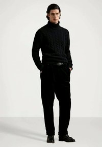 Sort kabelstrik højhalset sweater, parret med sorte fløjl bukser. Tætsiddende design, ribbede strukturer og sorte lædersko.